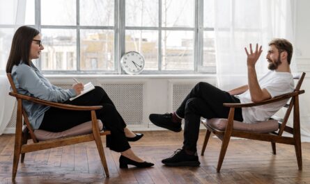 Person in Black Pants and Black Shoes Sitting on Brown Wooden Chair
