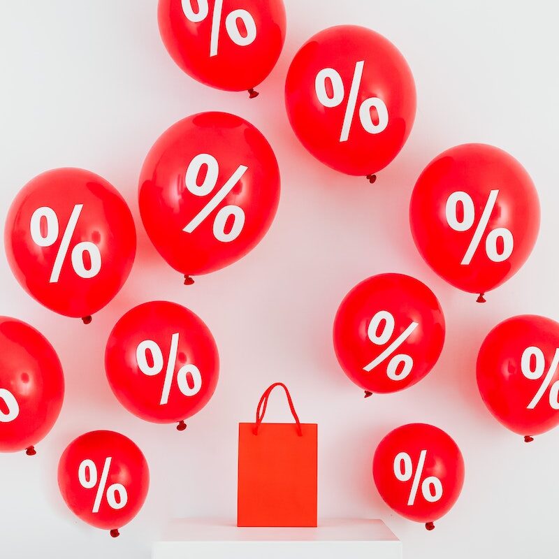 A Red Paper Bag in the Middle of Red Balloons With Percentage Symbols